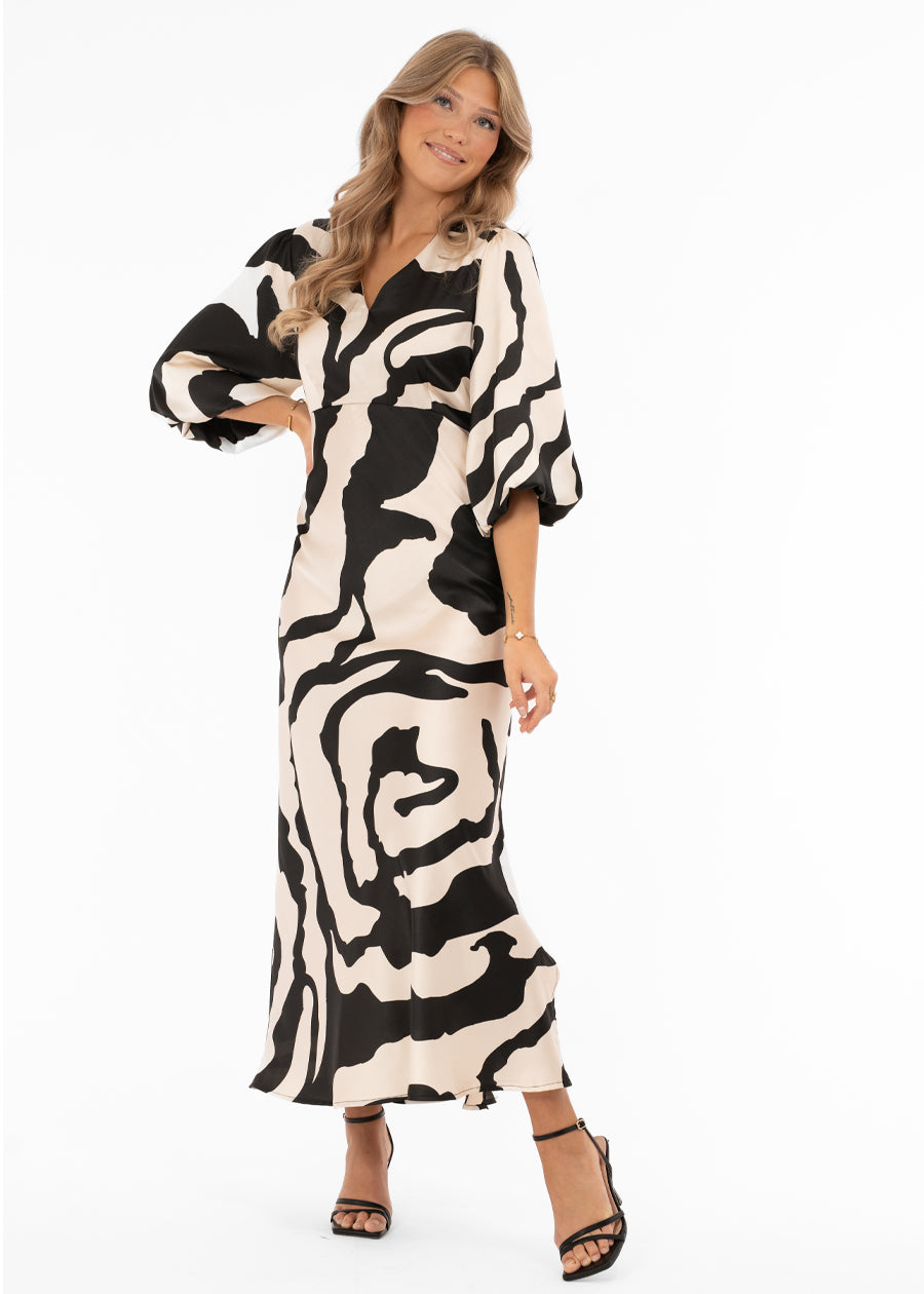 Naisten ylellinen satiinimekko shamppanjan sävyisellä pohjalla, musta abstrakti kuviointi, leveät puhvihihat, poikkileikkaus vyötäröllä, levenevä helma ja halkio toisella sivulla, V-pääntie