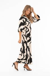 Naisten ylellinen satiinimekko shamppanjan sävyisellä pohjalla, musta abstrakti kuviointi, leveät puhvihihat, poikkileikkaus vyötäröllä, levenevä helma ja halkio toisella sivulla, V-pääntie