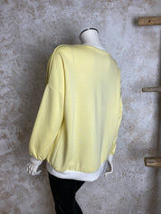 Naisten keltainen collegepaita pehmeästä ja joustavasta materiaalista, edessä “Have a nice day” -teksti, alaspäin kapeneva malli, pitkät hihat ja O-pääntie