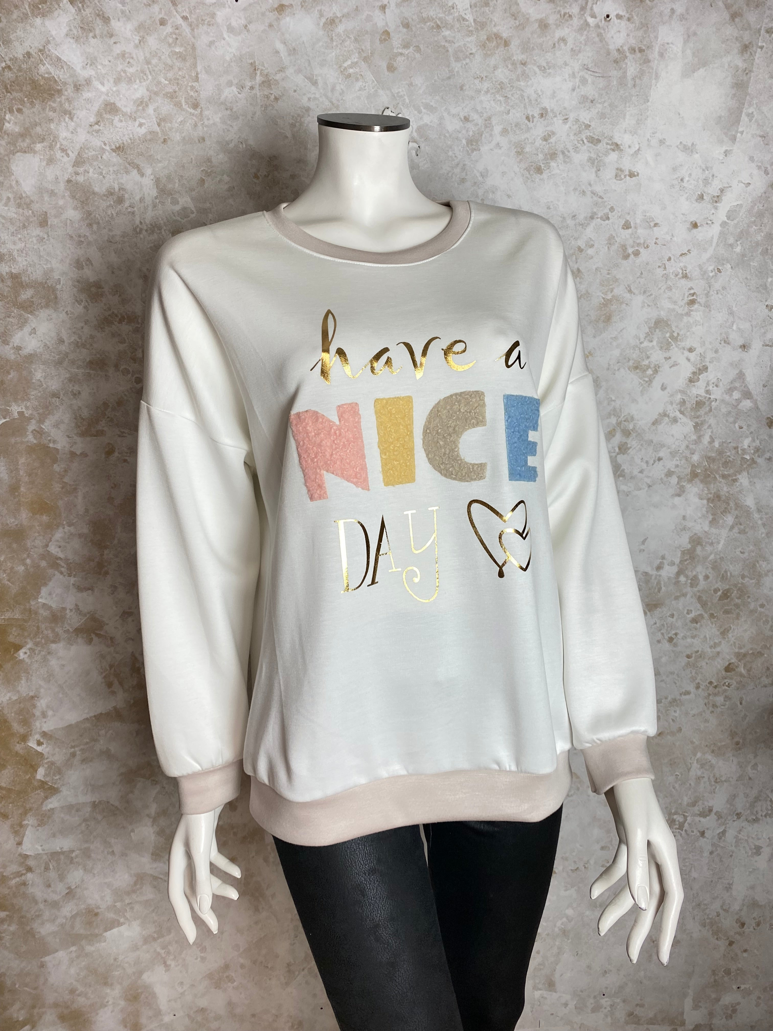 Naisten valkoinen collegepaita pehmeästä ja joustavasta materiaalista, edessä “Have a nice day” -teksti, alaspäin kapeneva malli, pitkät hihat ja O-pääntie