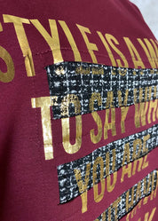 Naisellinen collegepaita, jossa kultainen teksti, koristeleikkaukset ja vohvelikangas helmassa, pehmeä ja joustava materiaali