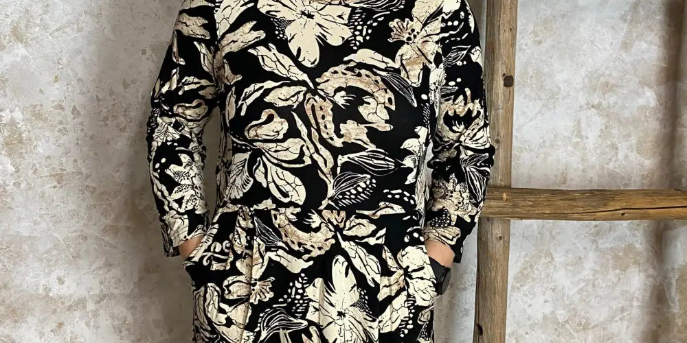 Hiekanvärinen kuviollinen mekko, jossa O-pääntie, vyötäröllä poikkileikkaus, taskut, vajaamittaiset hihat ja levenevä helma