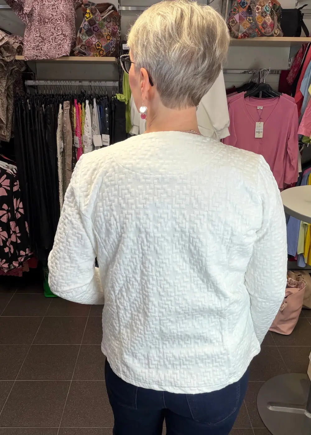 Valkoinen tekstuuripintainen neulosjakku paksusta joustavasta materiaalista, vetoketju edessä ja taskut