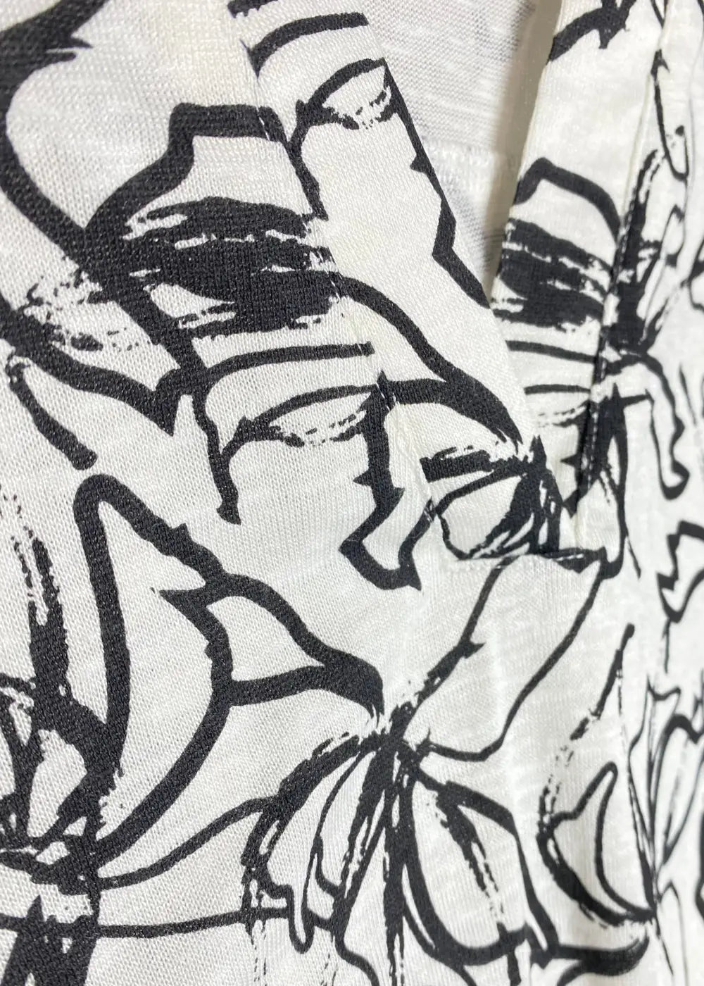 Naisten mustavalkoinen paitapusero joustavasta materiaalista, V-pääntie ja pieni kaulus, vajaamittaiset hihat ja kaareva helma